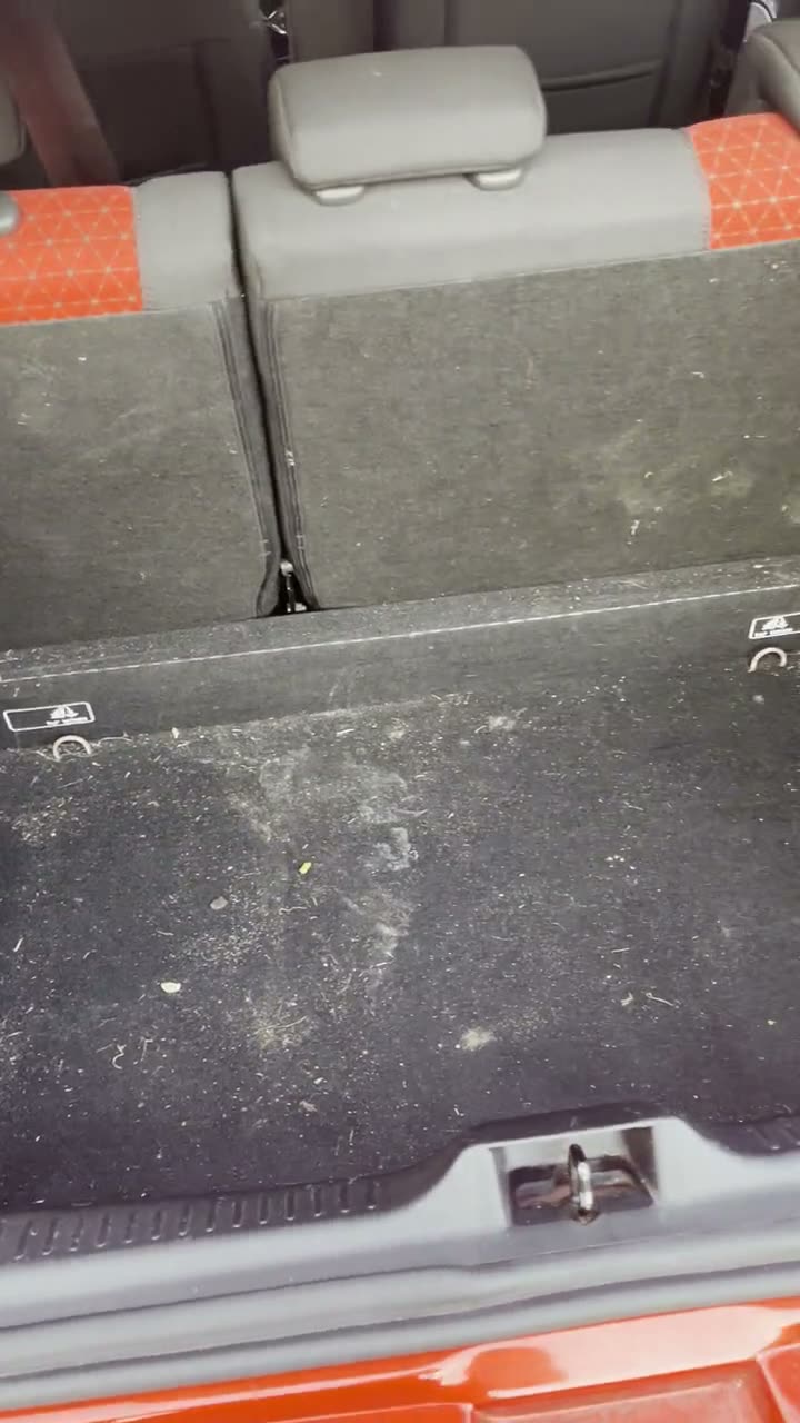Dirty boot carpet in a red Ford, covered in crumbs and debris before cleaning