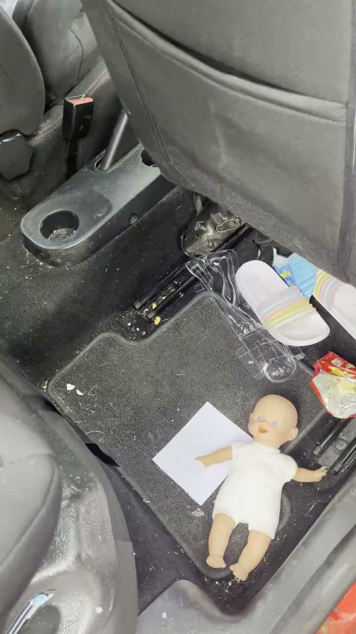 Dirty rear floor mat and carpet in a Ford, covered in crumbs and debris before cleaning