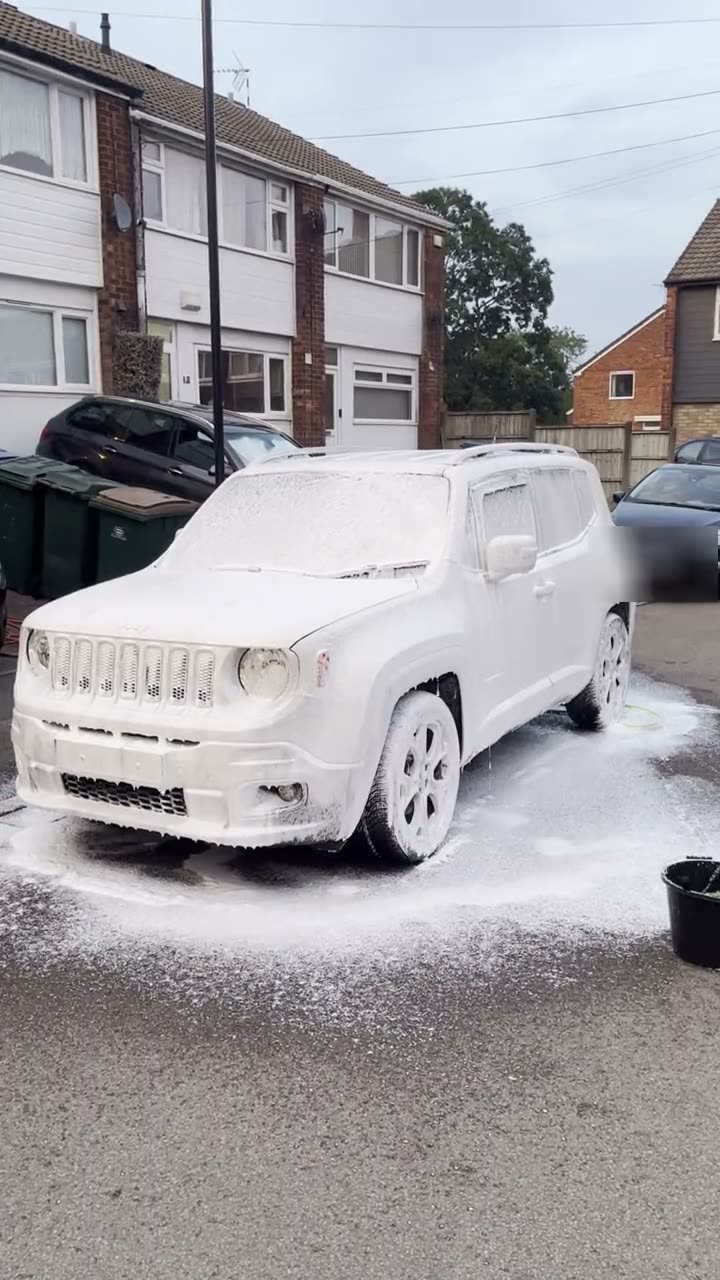 A Jeep covered in white snow foam during a mobile clean on a residential street