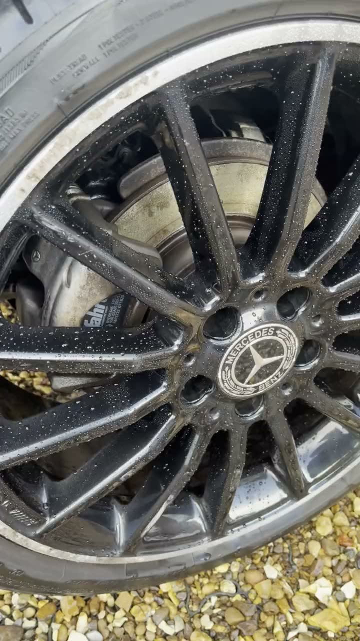 Close-up of a clean gloss black Mercedes alloy wheel on a gravel driveway, clean between the spokes