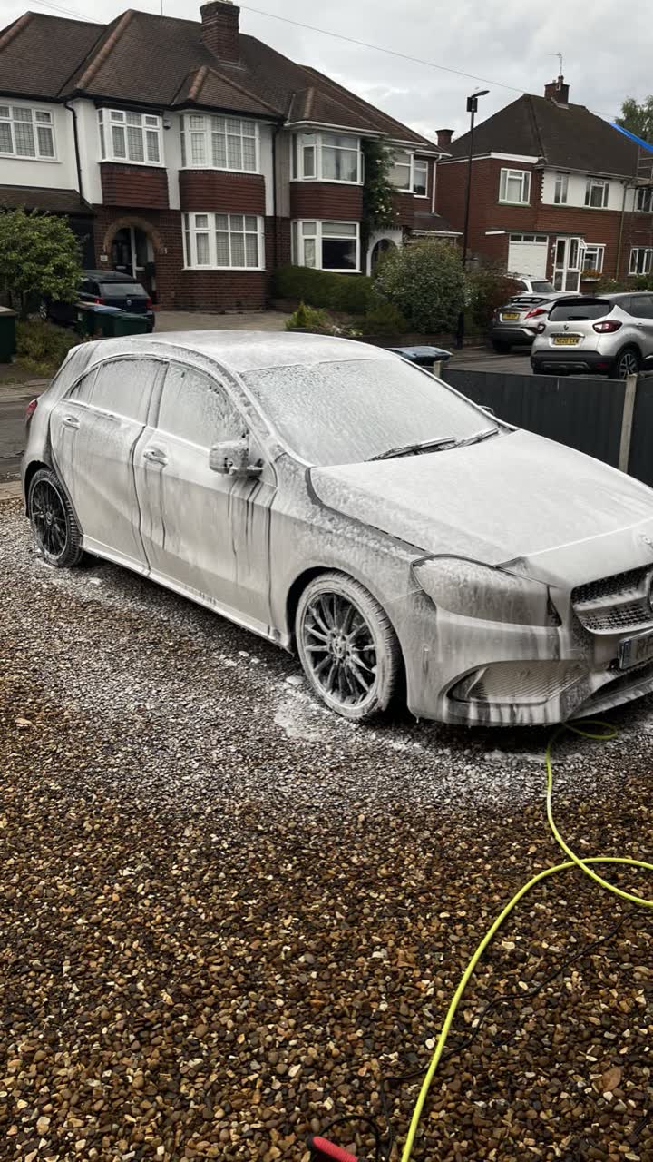 Silver Mercedes covered in white snow foam on a gravel driveway